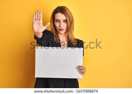 Redhead business caucasian woman holding banner over yellow isolated background with open hand doing stop sign with serious and confident expression, defense gesture