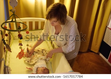 Young mother puts the baby to rest. Separate sleep infant and parents. Royalty-Free Stock Photo #1657017784