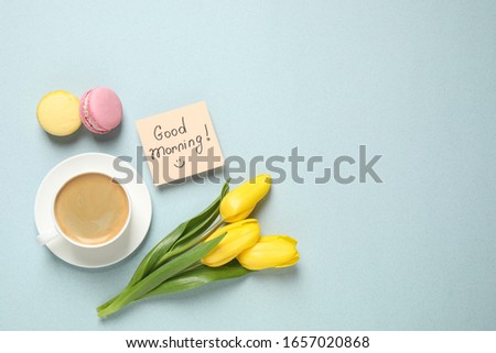 Delicious coffee, macarons, flowers and card with GOOD MORNING wish on light background, flat lay. Space for text