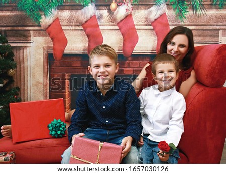 Beautiful brunette mom with her cute sons holding Christmas gifts and posing each other on red background at home. Happy childhood, parenthood, happy holiday and family concept.