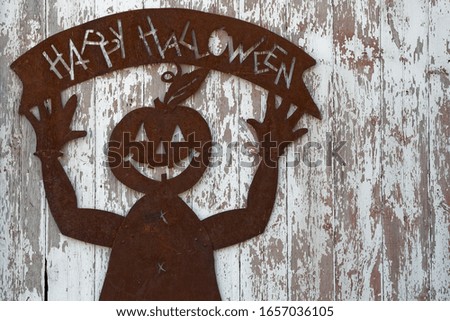 old rusted metal jack o lantern headed figure holding a happy halloween sign on the side of a rustic barn with peeling white paint