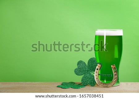 Green beer, horseshoe and clover leaves on wooden table, space for text. St. Patrick's Day celebration
