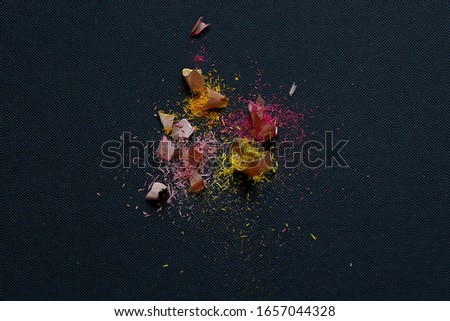 Colorful pencil's shavings are on the black fabric texture background close up taken with copy space around multicolor splash 