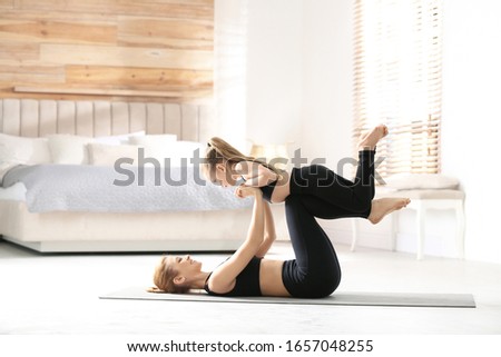 Mother and daughter in matching sportswear doing yoga together near bed at home
