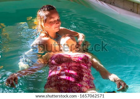 Beautiful senior woman receiving water massage in swimming pool from female therapist with sun rays falling on face in spa centre Royalty-Free Stock Photo #1657062571