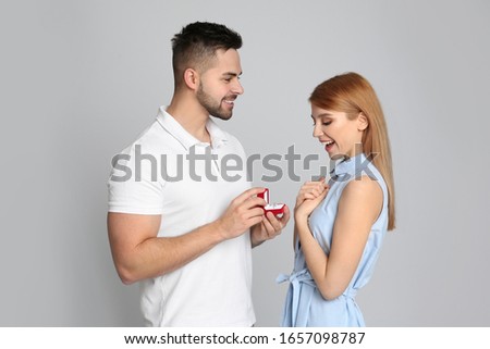 Man with engagement ring making marriage proposal to girlfriend on light grey background