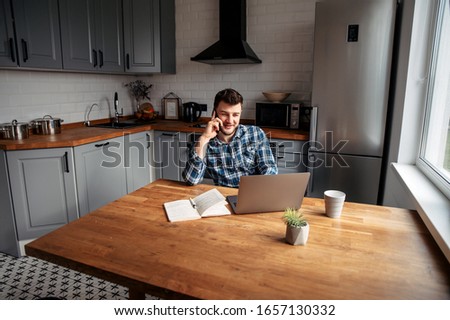 Work remotely. Young attractive hipster guy with a beard uses a laptop and a phone to work from home. Royalty-Free Stock Photo #1657130332
