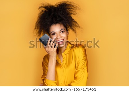 Girl uses the phone, leaves a voice message. Photo of african american girl on yellow background