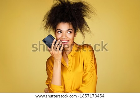 Cute girl uses the phone, leaves a voice message. Photo of african american girl on yellow background