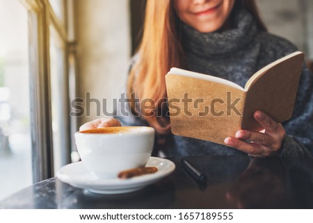 Closeup image of a beautiful woman reading a book while drinking coffee in the morning