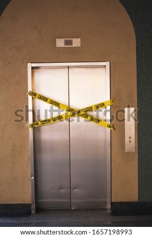 Out of service steel elevator with yellow warning tape,  caution for broken elevator