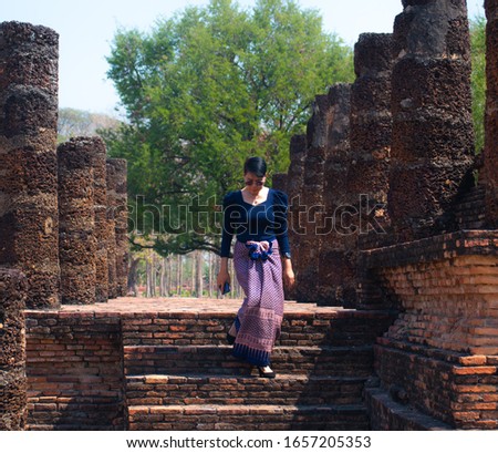 Adult woman in thai blue dress walking down from the old temple at Sukhothai Historical park, Sukhothai province northern of Thailand.