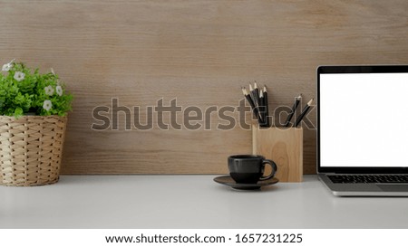 Close up view of contemporary workspace with blank screen laptop, stationery, cup, tree pot and copy space on white wooden desk