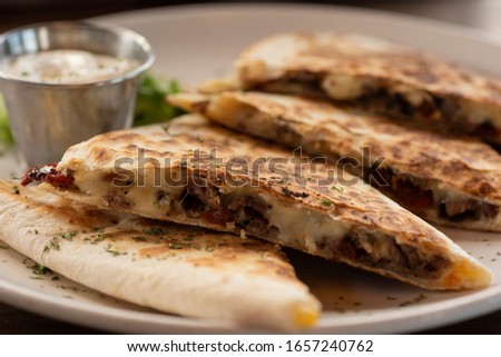 Selective focus steak quesadilla with Monterey Jack cheese, jalapeños, red chiles, and onions with sour cream on the side.