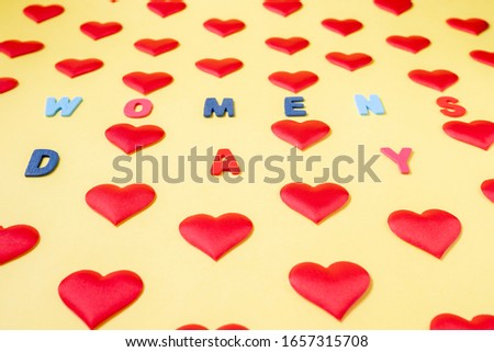 Multi-colored inscription, "Women's Day" in the middle of rhythmically arranged silk red hearts on a yellow background.  Postcard template for International Women's Day