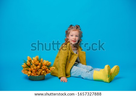 portrait of little  girl in a coat sitting and a bouquet of spring flowers on a colored blue background