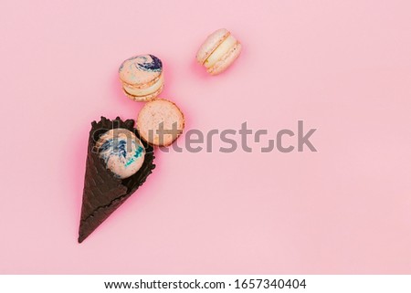 Assorted macaroons in black ice-cream horn on pastel pink background with copy space. Creative and moody picture.