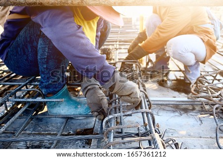 2 construction workers in clothing for sun protection equipment and working to tie the steel to create the main structure for pouring cement on the roof top, part of the construction of high building