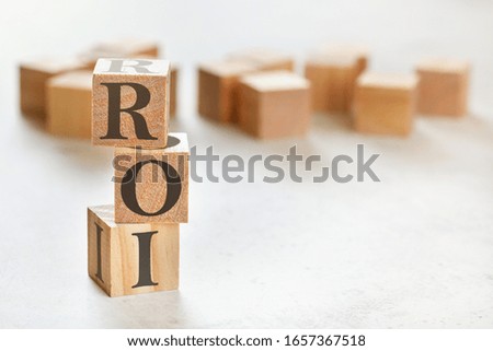Three wooden cubes with letters ROI (means Return on Investment), on white table, more in background, space for text in right down corner