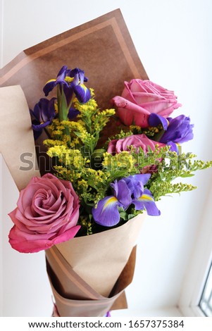 incredibly beautiful bouquet with large lilac-pink roses, iris and yellow flowers wrapped in craft paper. A beautiful present for a woman on International Women's Day.
