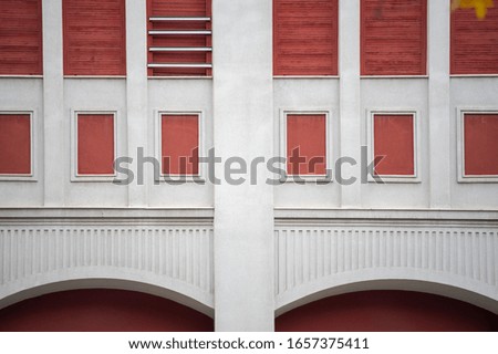 Architectural symmetric detail of old classy building with windows with red shutters and arches.