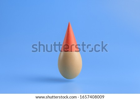 One brown egg  in a red festive cap on a blue background. Minimal Happy Easter concept decoration. Copy space for text mockup. Close up photography.