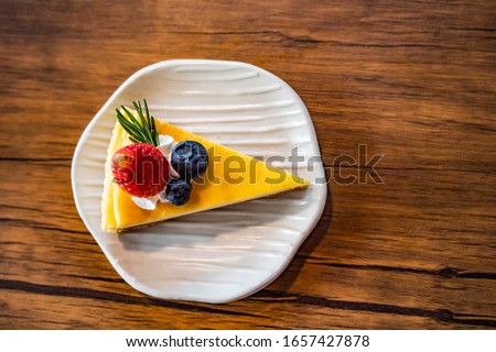 Triangle shaped cheesecake with fruit There are strawberries and blueberries placed on a wooden table. The picture above is beautiful.