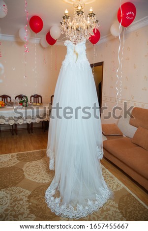 White wedding dress hangs on a chandelier in  room .The perfect wedding dress in the room of the bride . Wedding detail photography. Beautiful white wedding dress. Bridal morning