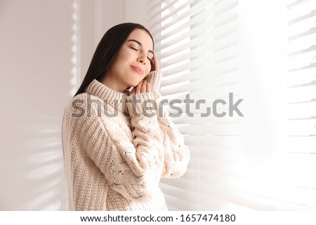 Young woman wearing warm sweater near window at home. Winter season