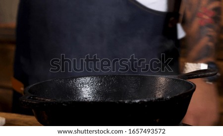 Close up of male chef frying ingredients in black iron pan and stirring them with a metal shovel. Stock footage. Process of food preparation.