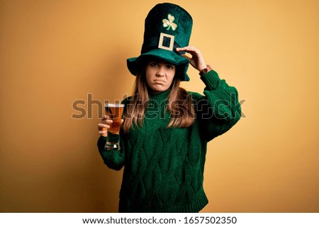 Young beautiful woman wearing green hat drinking glass of beer on saint patricks day worried and stressed about a problem with hand on forehead, nervous and anxious for crisis