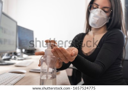 Corona Virus. Woman cleaning her hands at the office. Sick with mask for corona virus. Workplace desk with computer. Woman spraying alcohol gel or antibacterial soap sanitizer. Royalty-Free Stock Photo #1657524775