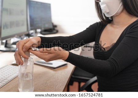Coronavirus. Woman cleaning her hands at the office. Sick with mask for corona virus. Workplace desk with computer. Woman spraying alcohol gel or antibacterial soap sanitizer. Royalty-Free Stock Photo #1657524781