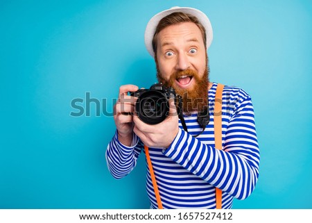 Portrait of excited man traveler have fun voyage weekend rest shooting professional camera wear white nautical vest orange suspenders isolated over blue color background
