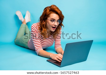 Full size close up photo crazy woman lie floor work laptop get incredible blogging notification impressed scream wow omg wear good look sneakers isolated blue color background
