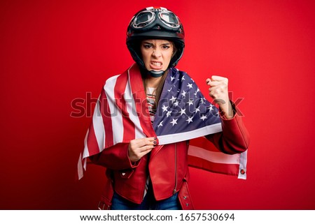 Young beautiful patriotic motorcyclist woman wearing motorcycle helmet and united states flag annoyed and frustrated shouting with anger, crazy and yelling with raised hand, anger concept
