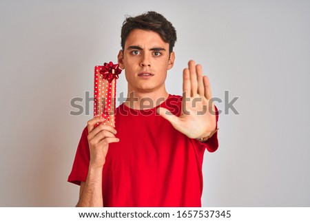 Teenager boy holding birthday gift over isolated background with open hand doing stop sign with serious and confident expression, defense gesture