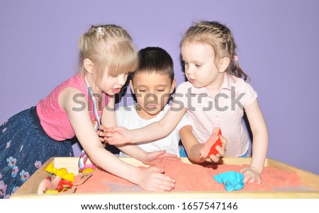 Two girls and a boy play with sand together
