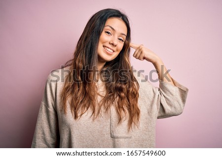 Young beautiful brunette woman wearing casual sweater standing over pink background Smiling pointing to head with one finger, great idea or thought, good memory