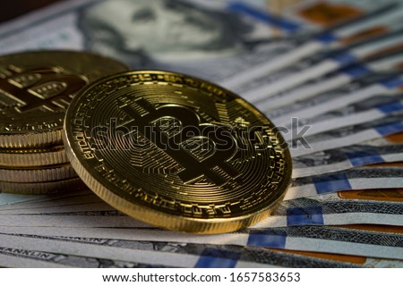 Gold coins in the form of bitcoin on a pile of hundred-dollar banknotes of a new sample