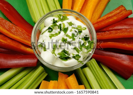 Slices of the carrot, celery, and red sweet pepper with a white vegan sauce laid out on a green dish