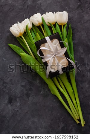 White tulip flowers and black gift box on dark background flat lay. Place for text 8 March Happy Womens Mothers Day.Flower Bouquet with silver ribbon, greeting card.Copy space website banner top view