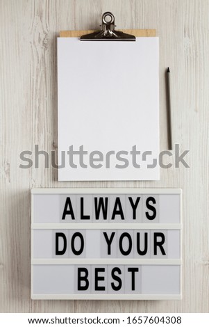 'Always do your best' words on a lightbox, clipboard with blank sheet of paper on a white wooden surface, top view. Overhead, from above, flat lay. 