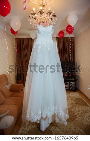 White wedding dress hangs on a chandelier in  room .The perfect wedding dress in the room of the bride . Wedding detail photography. Beautiful white wedding dress. Bridal morning