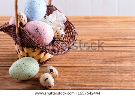 Festive Easter wicker basket with handmade painted chicken and quail eggs on a wooden table.