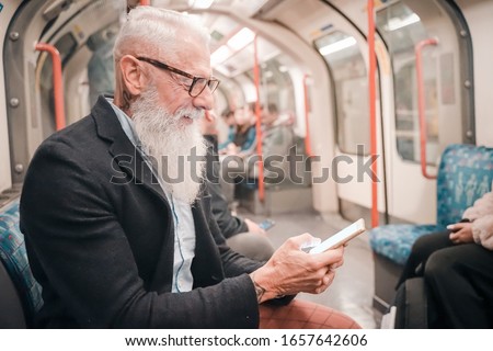 Pensioner playing with cellular phone sitting his train. Entrepreneur man using smartphone in subway underground. high iso. Holiday, work and lifestyle concept - Image