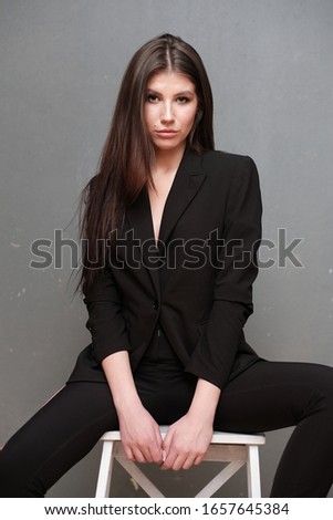 Close-up portrait of a beautiful cute girl with long hair and in a black jacket on a gray background. Girl posing for the photographer in a photo studio.