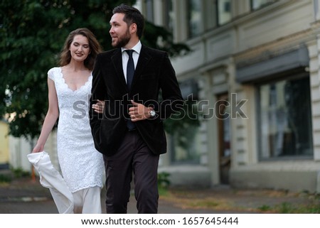 Beautiful wedding couple of newlyweds - red-haired young bride in a white dress and a bearded groom in a black suit. Amazing smiling wedding couple. Pretty bride and stylish groom.