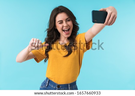 Image of emotional happy optimistic young pretty woman posing isolated over blue wall background take selfie by mobile phone pointing to herself.
