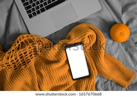 Stay Home In Isolation And Watch Online Movie and TV Series. Mobile Phone With Blank Screen On Woolen Sweater Near Orange And Laptop. Copy Space. Empty Space.